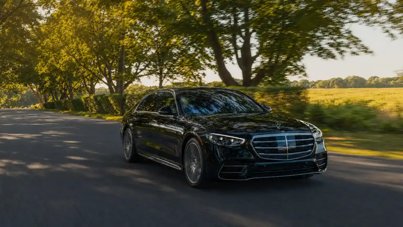 NYC to the Hamptons Car Service 7 Black Mercedes sedan on a tree-lined Long Island road heading to the Hamptons at golden hour
