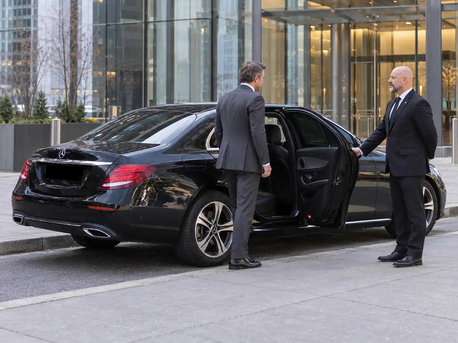 Chauffeur opening the rear door of a black Mercedes sedan for an executive outside a Manhattan office tower