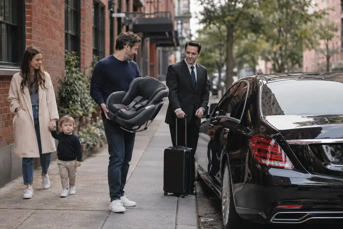 Parent carrying the family car seat to a black sedan while the chauffeur waits on a Tribeca sidewalk